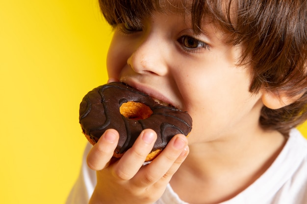 A front view little cute boy eating donuts