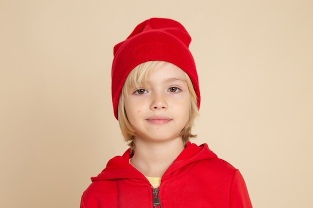 Vista frontale ragazzino carino in camicia rossa e berretto sorridente sul muro bianco