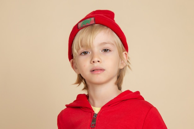 Front view little cute boy in red shirt and cap on white wall