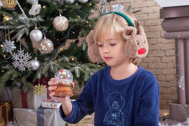 Front view little cute boy sitting around xmas tree and presents