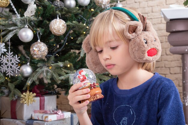 Front view little cute boy sitting around xmas tree and presents