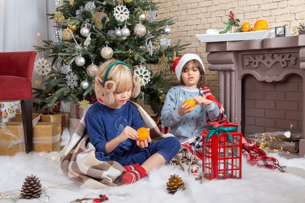 正面図クリスマスツリーの周りに座って、タンジェリンの子供色の新年の写真の子供時代のクリスマスを食べて彼らの家にプレゼントする小さなかわいい男の子
