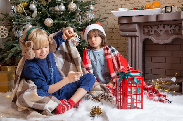 Front view little cute boys sitting around xmas tree and presents in their house