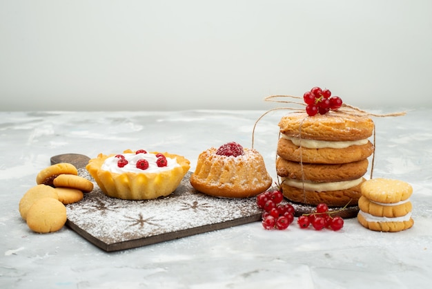 Бесплатное фото Вид спереди маленькие пирожные со сливками и сэндвич-печеньем на светлой поверхности, сахарная сладость