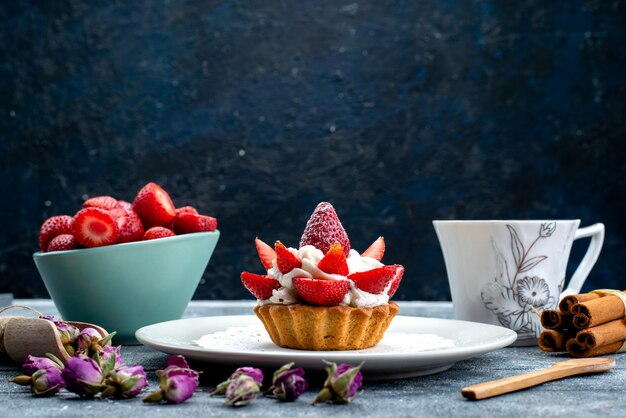 A front view little delicious cake with cream inside plate with fresh sliced strawberries and tea on the blue-grey background cookie biscuit cake fruit 