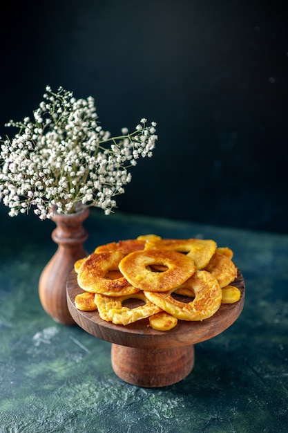 Вид спереди маленькие вкусные пирожные в форме кольца ананаса на темном фруктовом пироге, выпечка, цветная выпечка