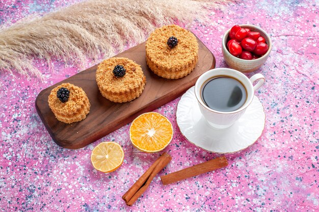 Front view of little delicious cakes with cinnamon and cup of tea on light pink surface