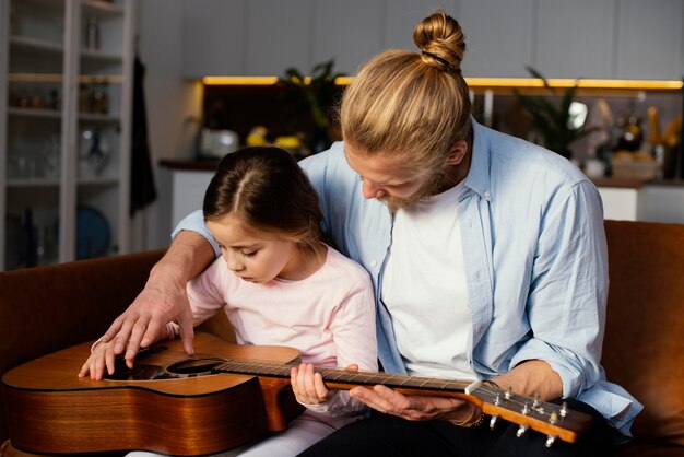 Front view of little girl and father playing guitar together