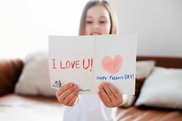 Вид спереди маленькой девочки, держащей открытку на день отца как сюрприз для ее отца