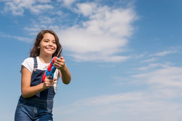 Front view little girl playing with water gun outside