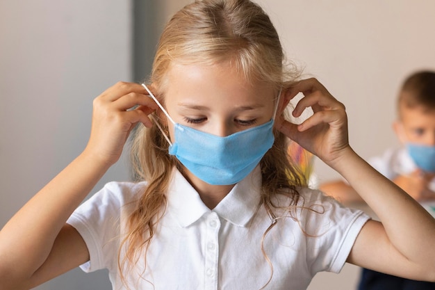 Front view little girl putting on a face mask