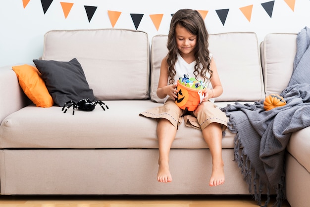 Free photo front view little girl sitting on couch on halloween