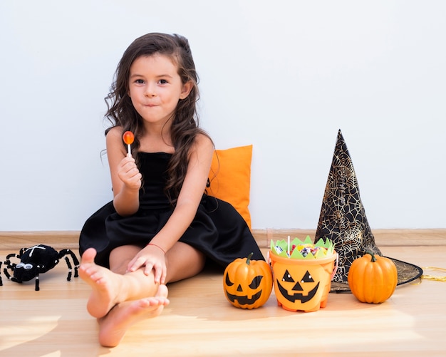 Вид спереди маленькая девочка, сидя на полу на Хэллоуин