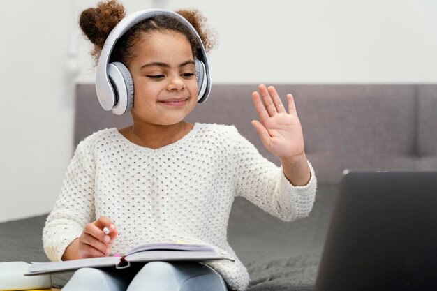 Front view of little girl waving and using laptop for online school