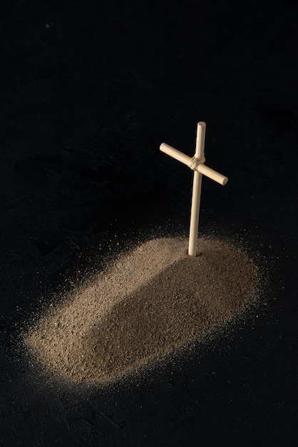 Front view of little grave from sand with stick cross on black