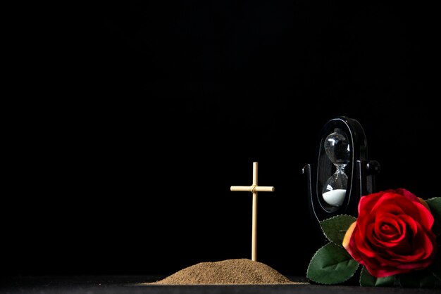 Front view of little grave with hourglass and red rose on black