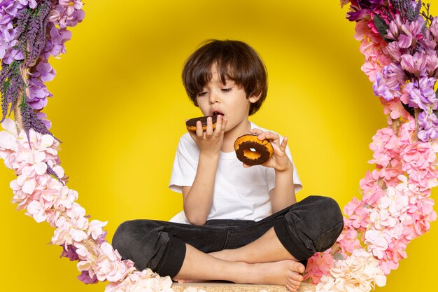 A front view little kid adorable sweet eating choco donuts on the yellow space