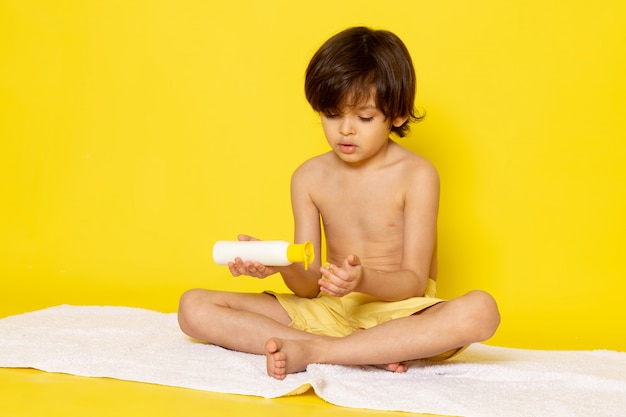 Free photo front view little kid using cream on yellow