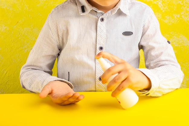 Vista frontale ragazzino utilizzando spray come misura di prevenzione sulla superficie gialla