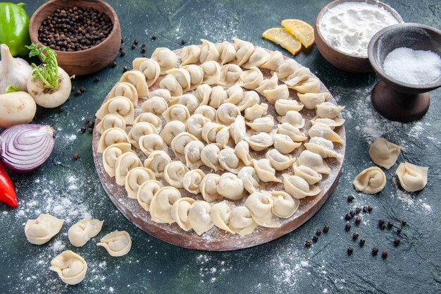 Front view little raw dumplings with flour on dark gray surface