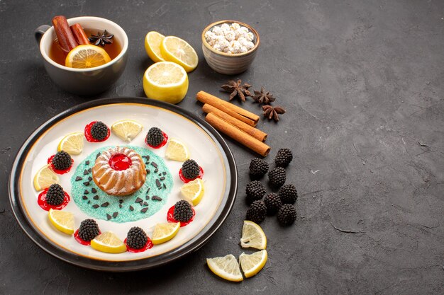 Front view little yummy cake with lemon slices and cup of tea on dark background fruit citrus cookie biscuit sweet