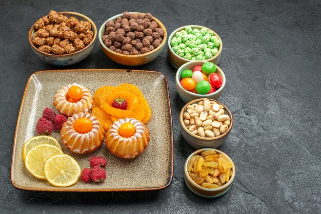 Вид спереди маленькие вкусные пирожные с конфетами и орехами на сером пространстве