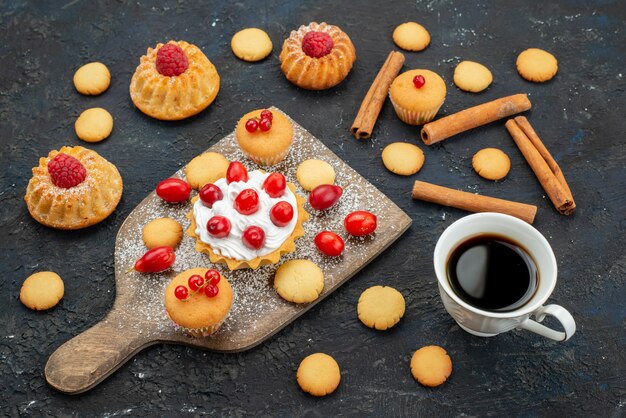 Вид спереди маленькие вкусные пирожные со сливками, корицей, кофе и свежими фруктами на темной поверхности, сладкое печенье, торт, десерт, фрукты, ягоды