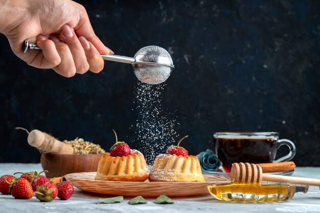 Вид спереди маленькие вкусные пирожные с красной клубникой, корицей и бисквитом с чаем