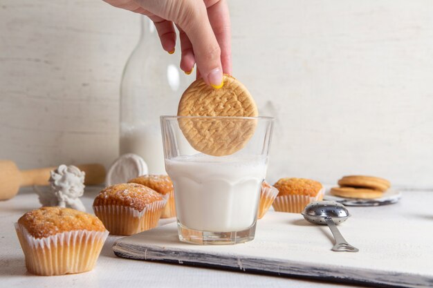 Front view of little yummy cakes with sugar powder and female dunking cookie inside milk