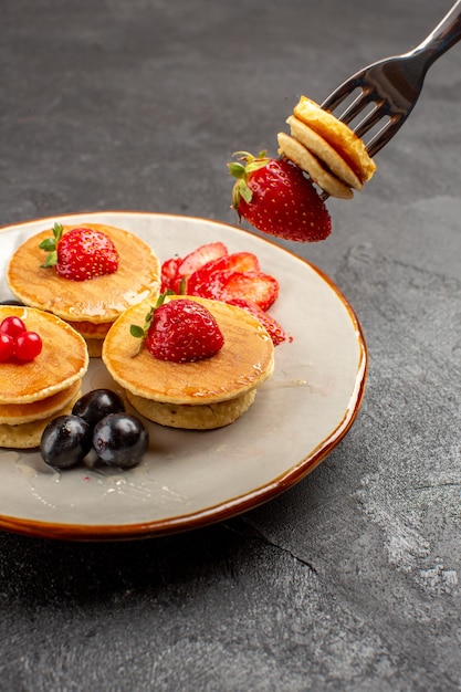 Foto gratuita vista frontale piccole frittelle gustose con frutta sulla frutta torta torta superficie grigia