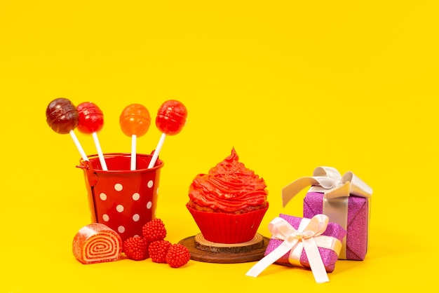 A front view lollipops and cake with marmalade and purple gift boxes on yellow, color sugar biscuit