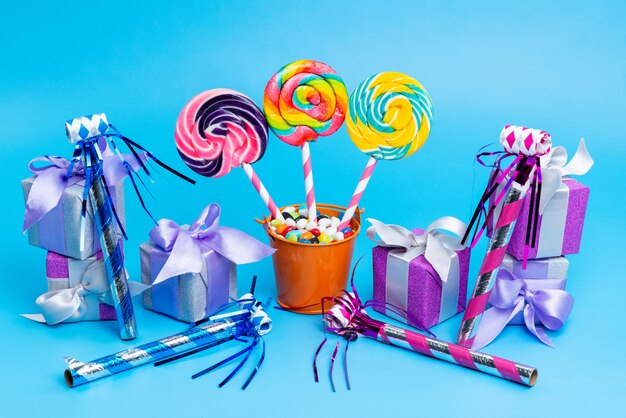 A front view lollipops and candies with little gift boxes birthday whistles on blue