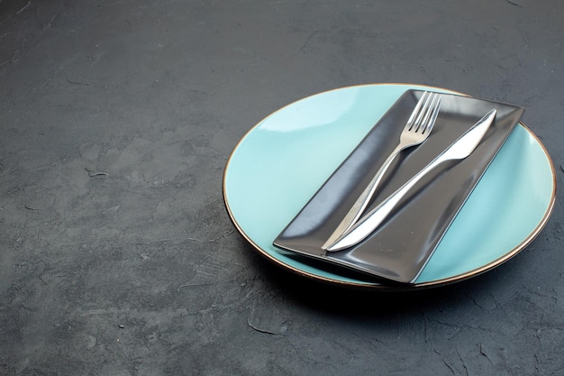 Вид спереди длинная черная тарелка с синей тарелкой, вилкой и ножом на темноте