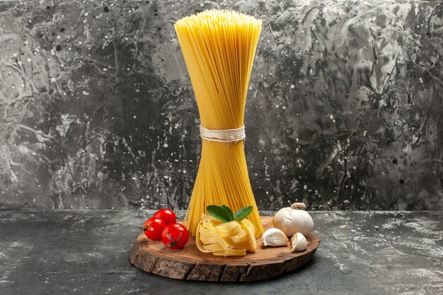 Front view long italian pasta with red tomatoes and garlic on light-grey food color dough cuisine photo meal