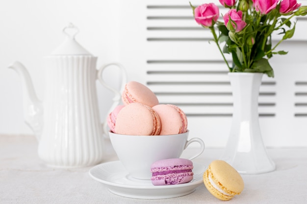 Front view of macarons in cup with roses in vase