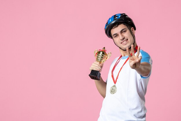 Front view male athlete in sport clothes holding golden cup with helmet