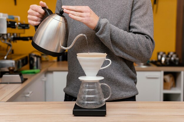 Front view of male barista pouring hot water over coffee filter