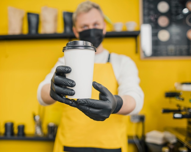 Front view of male barista with medical mask and gloves holding coffee cup