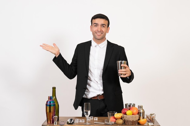 Front view male bartender in classic suit standing in front of table with drinks on the white wall alcohol club drink male night bar