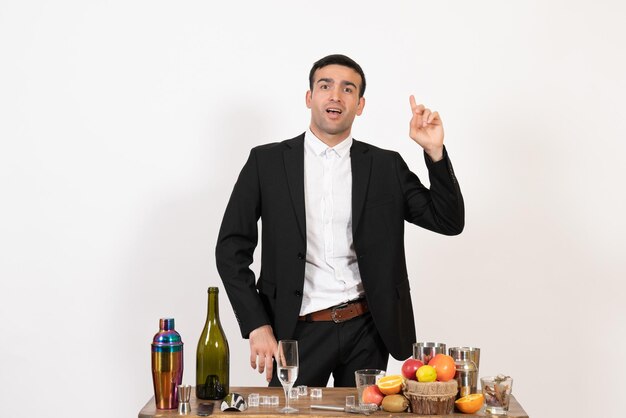 白い壁のクラブの男性のナイトバーの飲み物アルコールと飲み物とテーブルの前に立っている古典的なスーツの正面図男性バーテンダー