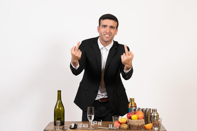 Front view male bartender in classic suit standing in front of table with drinks on a white wall male alcohol club drink bar night