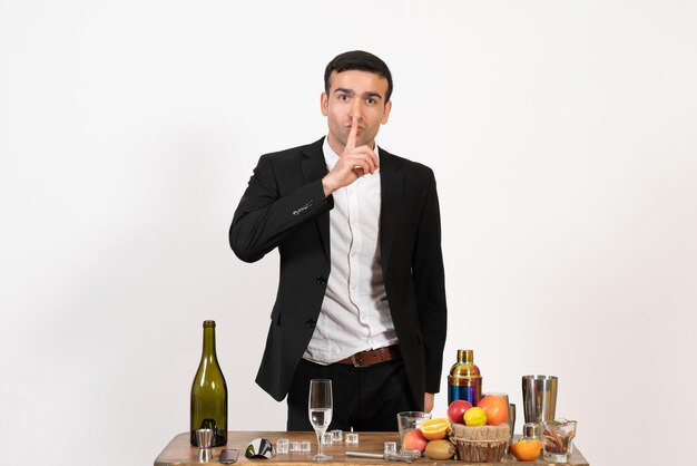 Front view male bartender in classic suit standing in front of table with drinks on white wall night male club bar alcohol drink