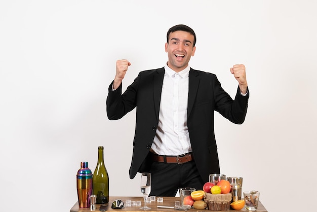 Front view male bartender in classic suit standing and rejoicing on white wall night club male bar drink alcohol