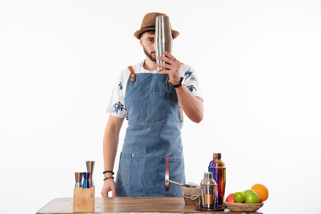 Front view male bartender in front of bar desk preparing a drink in shaker on a white wall bar alcohol job fruit drink club night