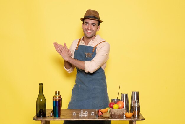 Free photo front view male bartender in front of table with drinks and shakers clapping on yellow wall night alcohol male drink club bar