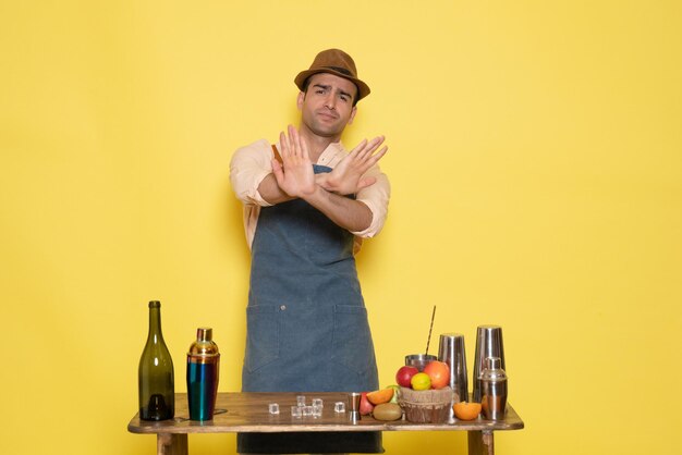 Front view male bartender in front of table with drinks and shakers on yellow desk drink night alcohol bar color club