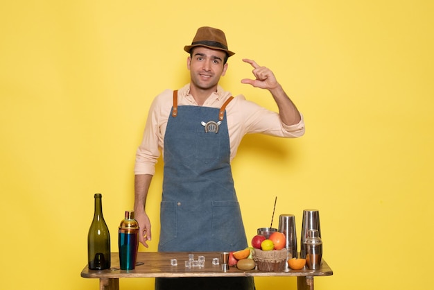 Free photo front view male bartender in front of table with drinks and shakers on a yellow wall drink night alcohol bar color club male