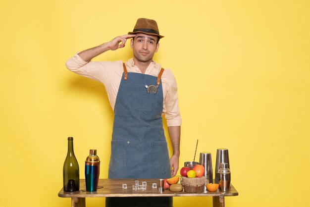 Front view male bartender in front of table with drinks and shakers on yellow wall drink night alcohol bar color club