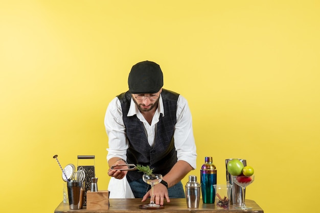 Free photo front view male bartender in front of table with shakers making drink on yellow floor bar alcohol drink night club youth