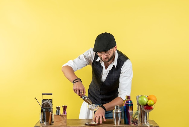 Free photo front view male bartender in front of table with shakers preparing drink on yellow wall bar alcohol drink night club youth